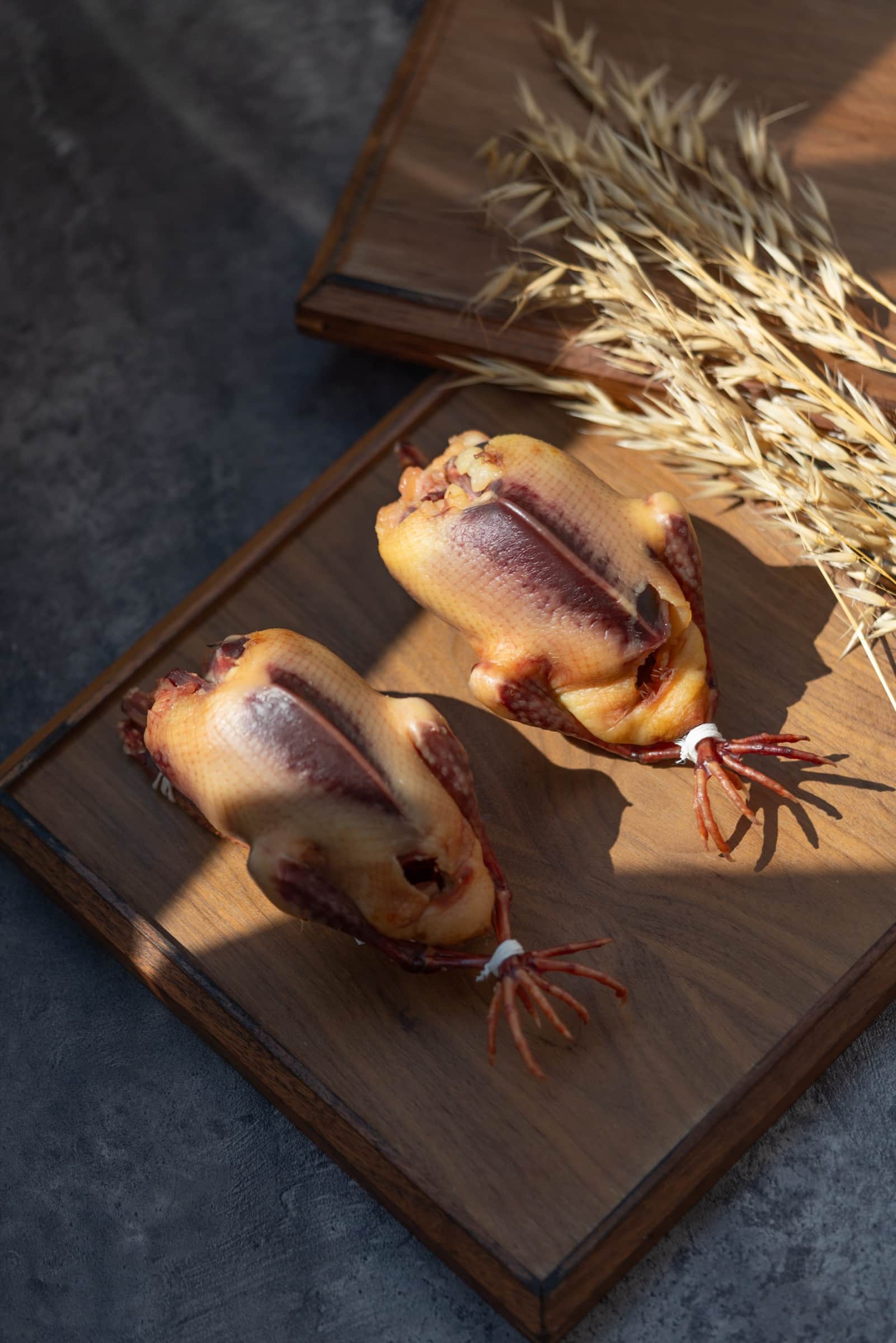 Whole poussin tied with twine, presented on a dark wood board with dried wheat